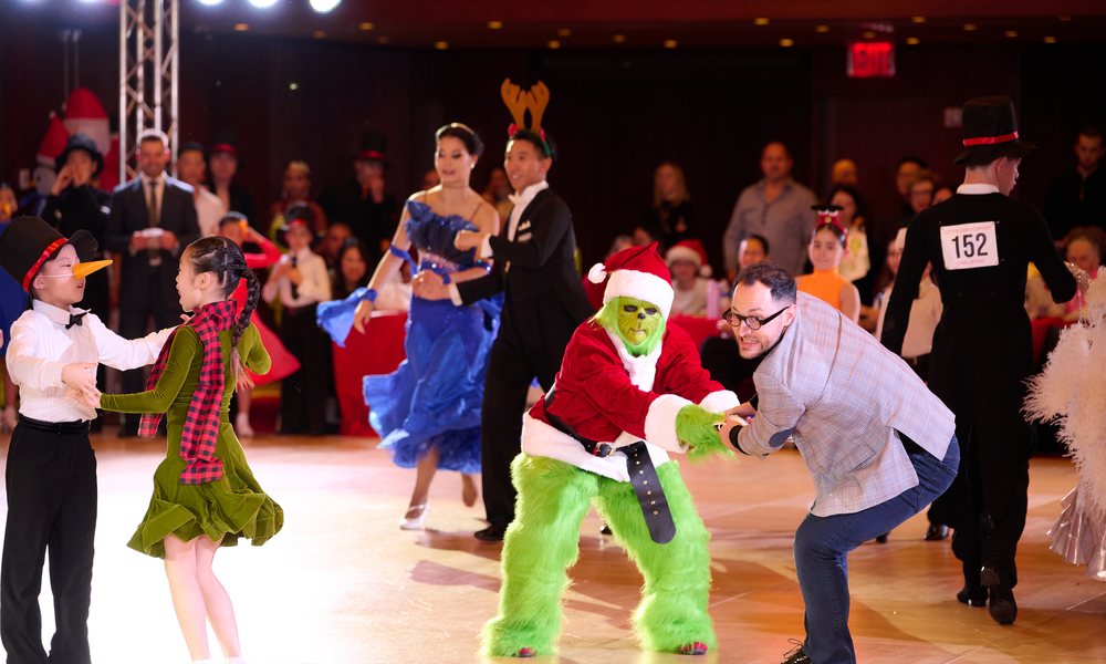 A costumed Grinch dancing with a child on the floor at City’s Dancesport Challenge